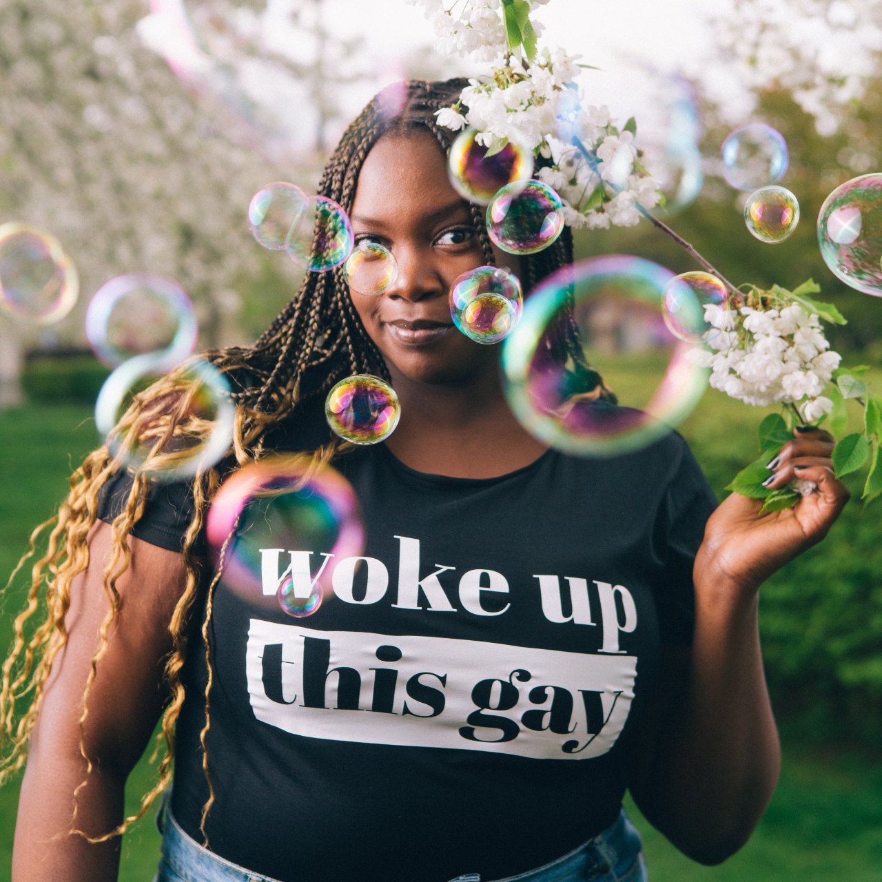 T-shirt Woke up this Gay, modell som står under träd med vita blommor. Såpbubblor skymmer lite av bilden.