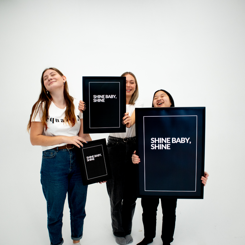 Poster Shine, inramad, alla tre storlekar hålls upp av tre unga kvinnor som ler