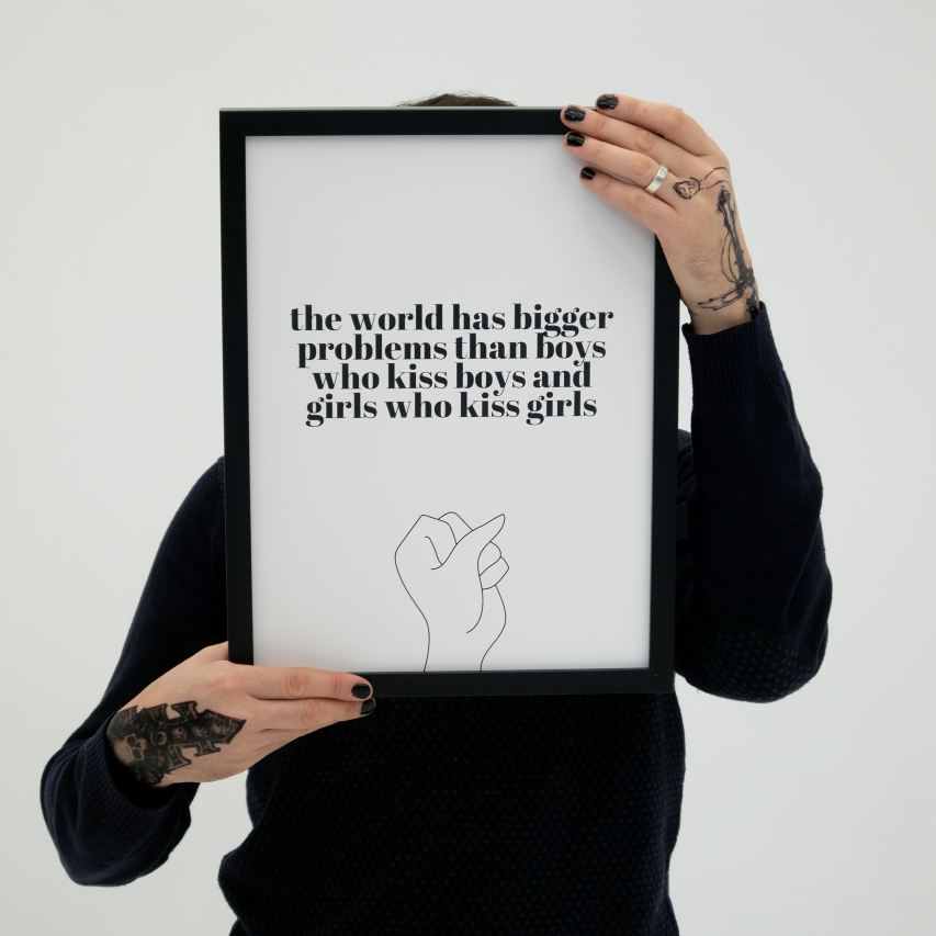 Poster The world, vit med svart text. Håll upp av person med tatuerade händer. Ansiktet är skymt bakom tavlan.