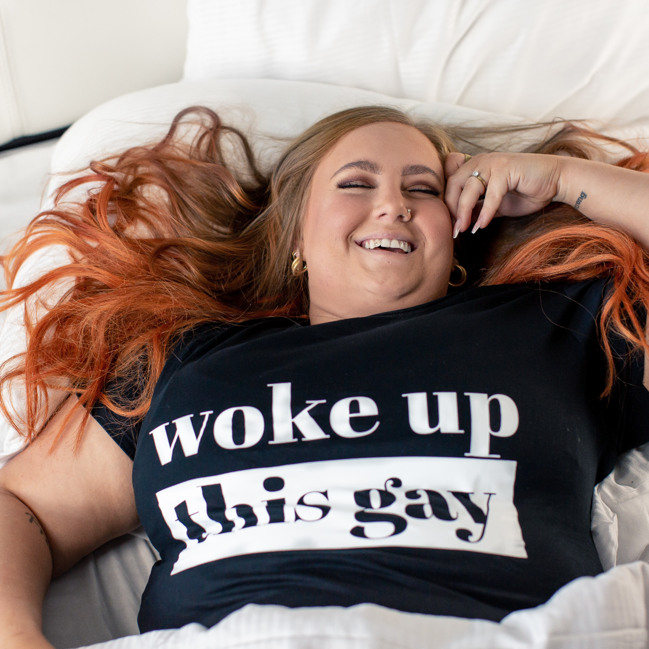 T-shirt Woke up this Gay, modell ligger i sängen med håret utslaget över kuddarna 