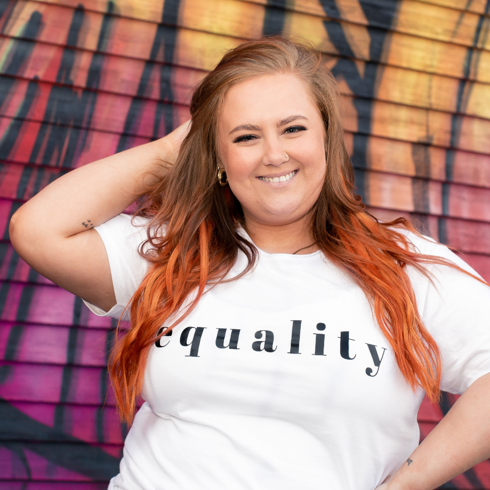 T-shirt Equality, kvinnlig modell med vit t-shirt framför vägg med graffiti