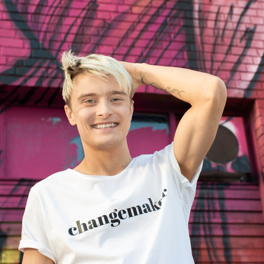 T-shirt Changemaker. Manlig modell i vit t-shirt med en vägg med graffiti i bakgrunden