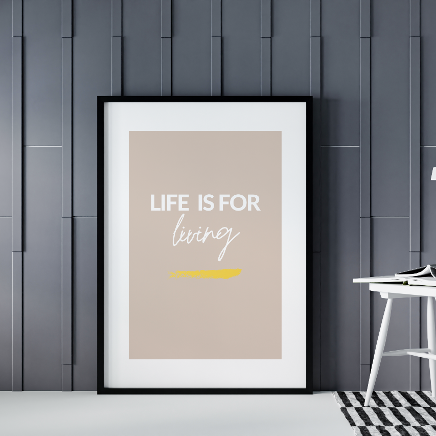 Poster Life is for living, med guldfoliering, inramad mot grå vägg. Till höger syns en vit stol