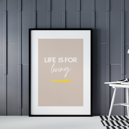 Poster Life is for living, med guldfoliering, inramad mot grå vägg. Till höger syns en vit stol