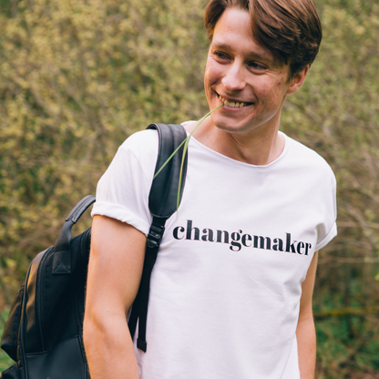 T-shirt Changemaker. Manlig modell i vit t-shirt med ryggsäck på axeln och grässtrå i munnen 