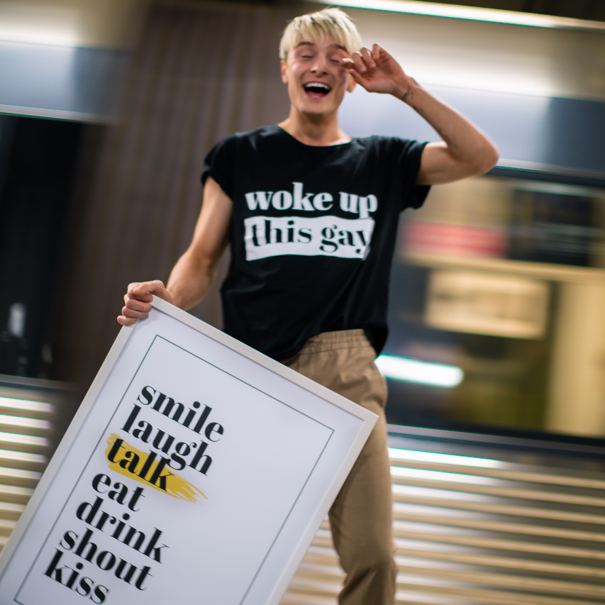 Poster sju budord inramad. Yngre man håller den framför sig medan ett tunnelbanetåg kör förbi i bakgrunden