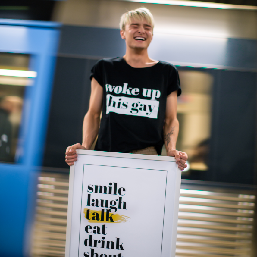 Poster sju budord inramad. Yngre man håller den framför sig medan ett tunnelbanetåg kör förbi i bakgrunden