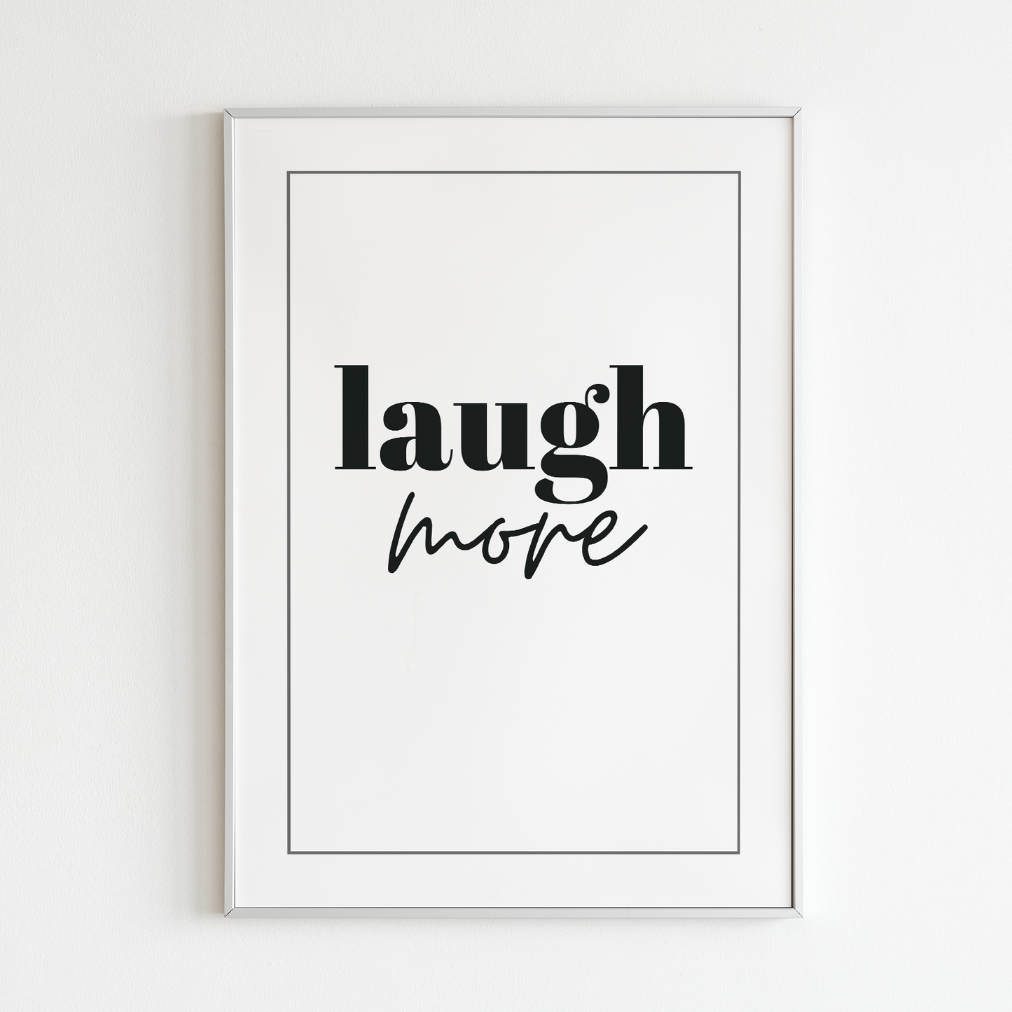 Poster Laugh more, vit med svart text, inramad mot vit vägg.