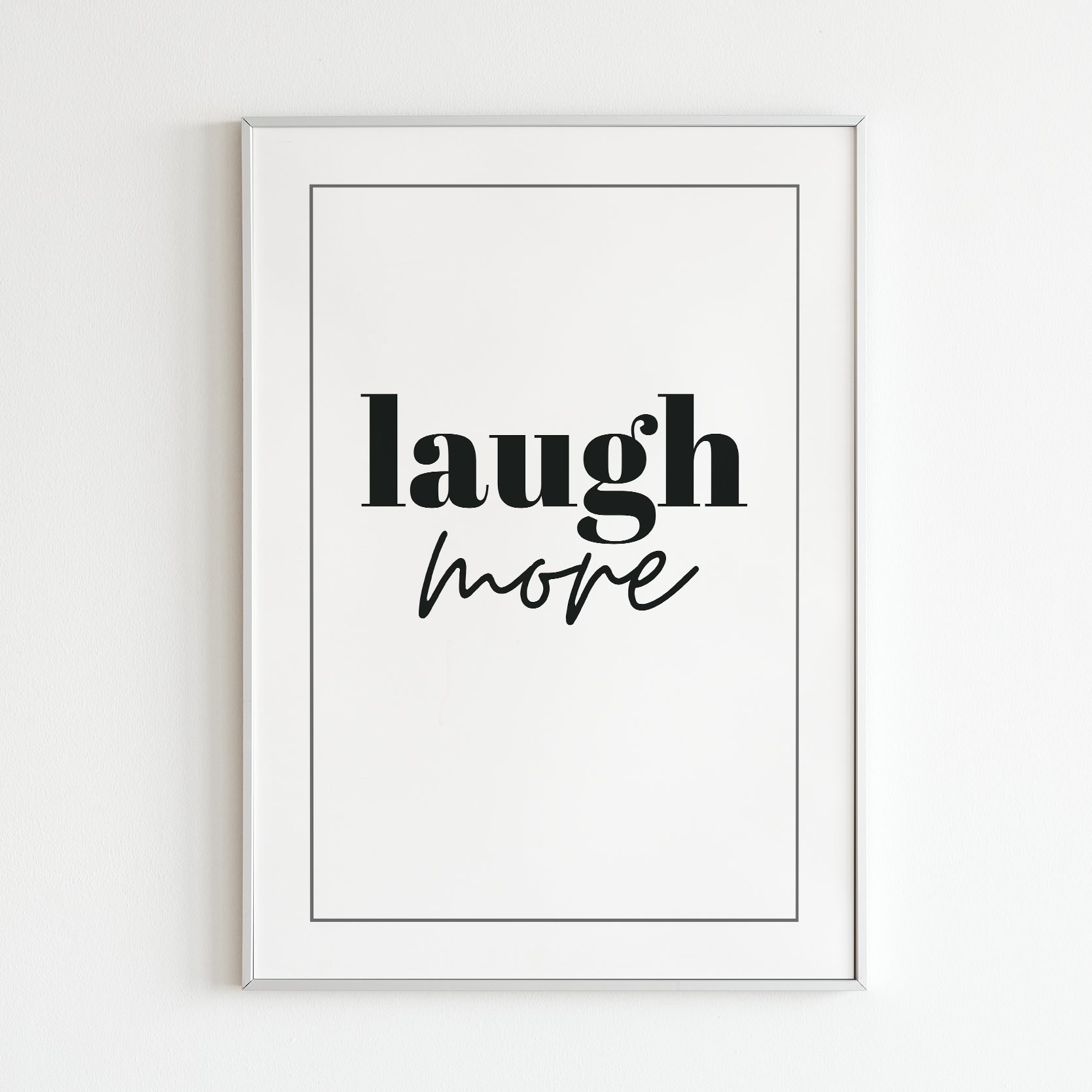 Poster Laugh more, vit med svart text, inramad mot vit vägg.