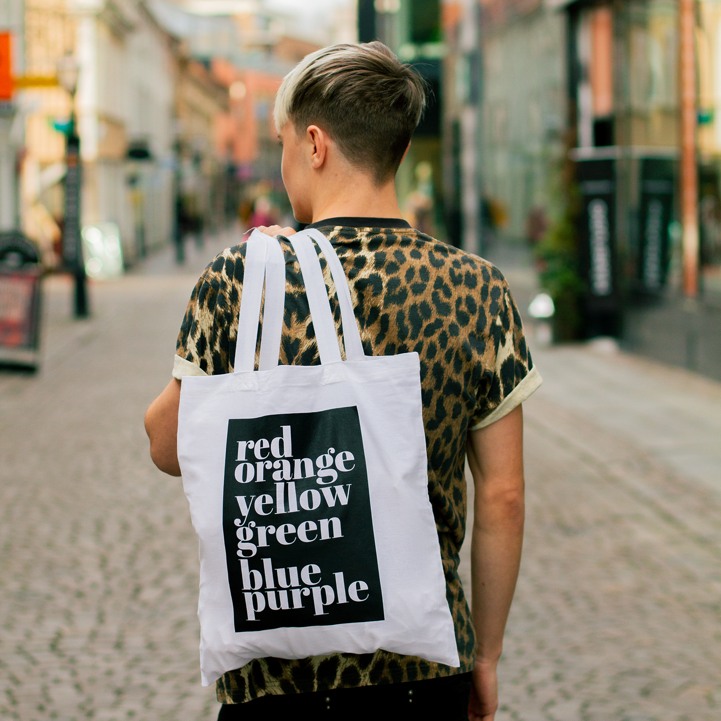 Tygkasse Rainbow, hålls över ryggen av modell, i stadsmiljö