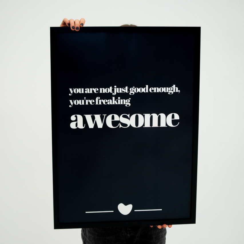 Poster Freaking Awesome inramad hålls upp en person med svarta naglar.