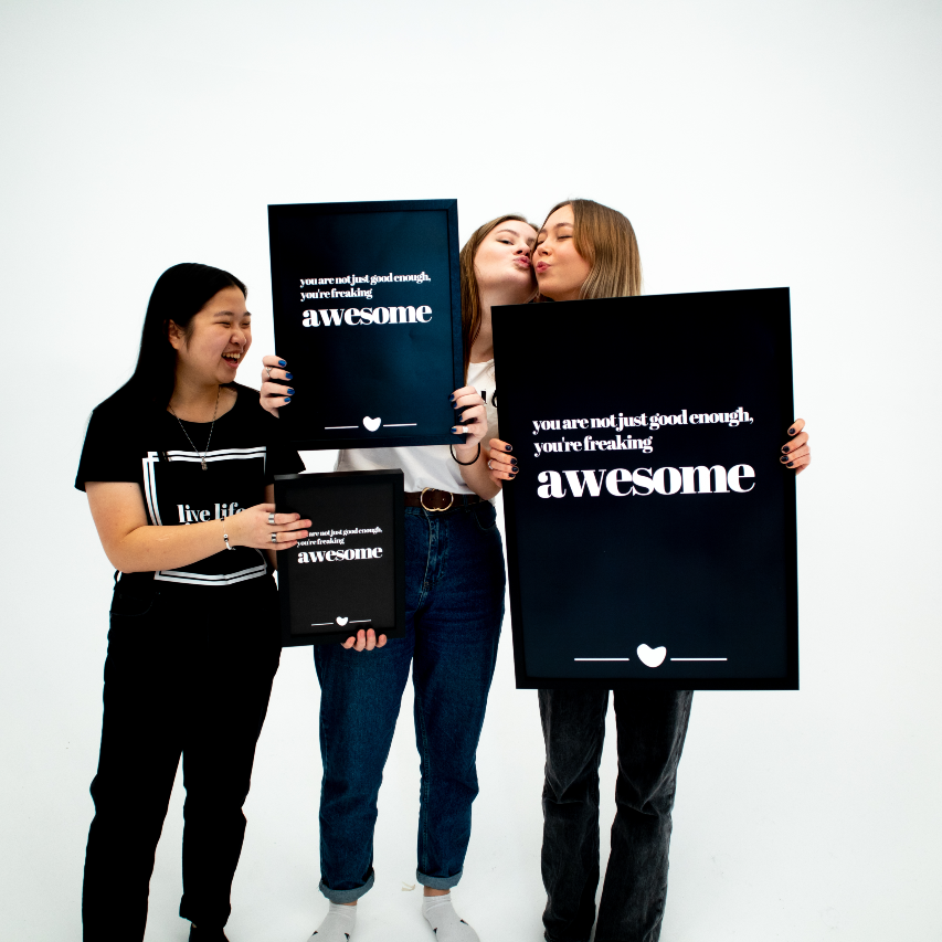 Poster Freaking awesome tre storlekar och inramade hålls upp av tre personer