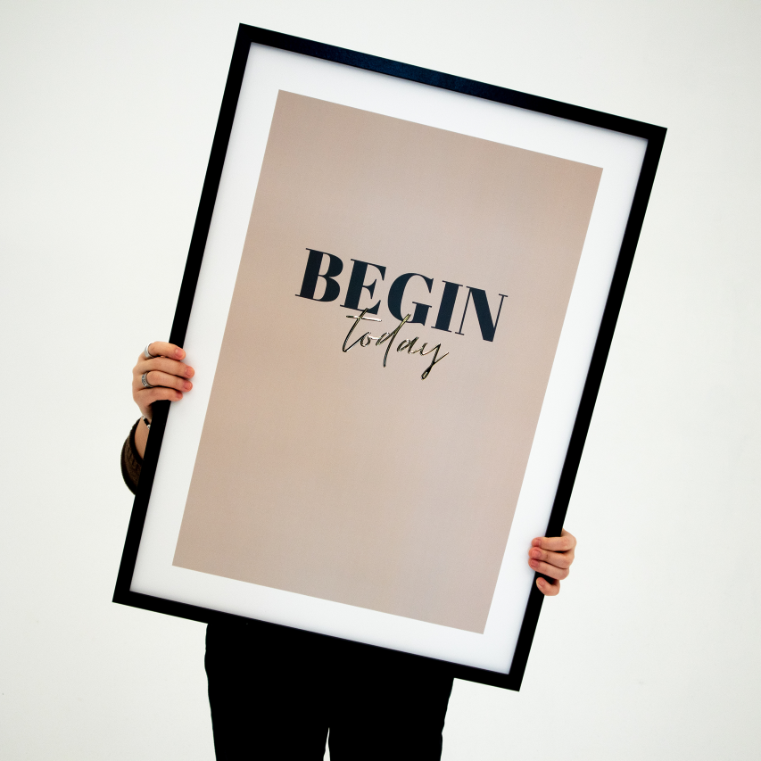Poster Begin today, inramad. En person håller upp tavlan framför sig.
