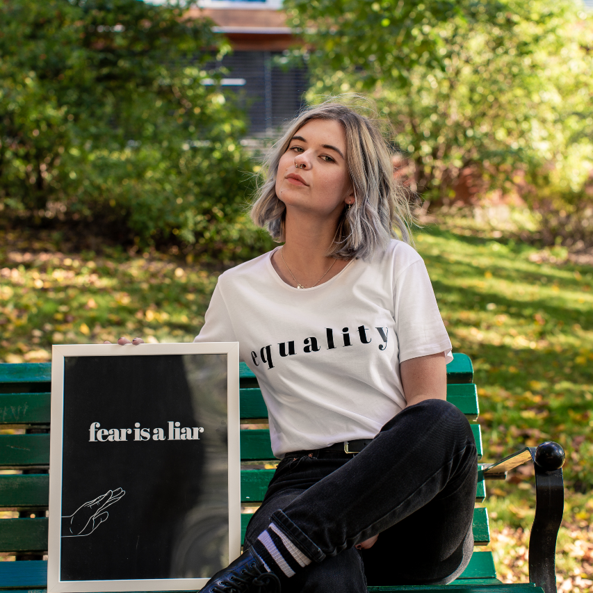 Poster Fear is a liar hålls av kvinna på parkbänk med grönska i bakgrunden