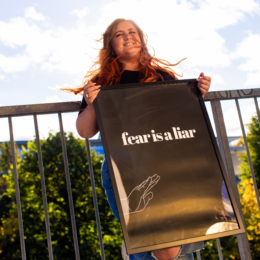 Poster Fear i a liar inramad hålls upp av en kvinna med yvigt rött hår