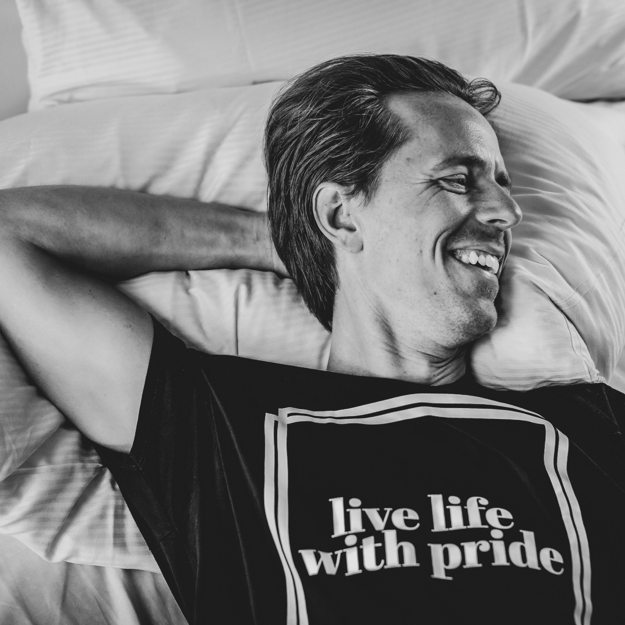 T-shirt Live Life modell ligger i sängen med en arm under huvudet.