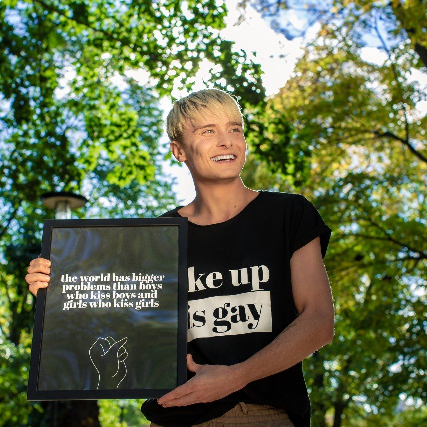 Poster The world, svart med vit text, hålls upp av en ung man som ler med solen i ansiktet