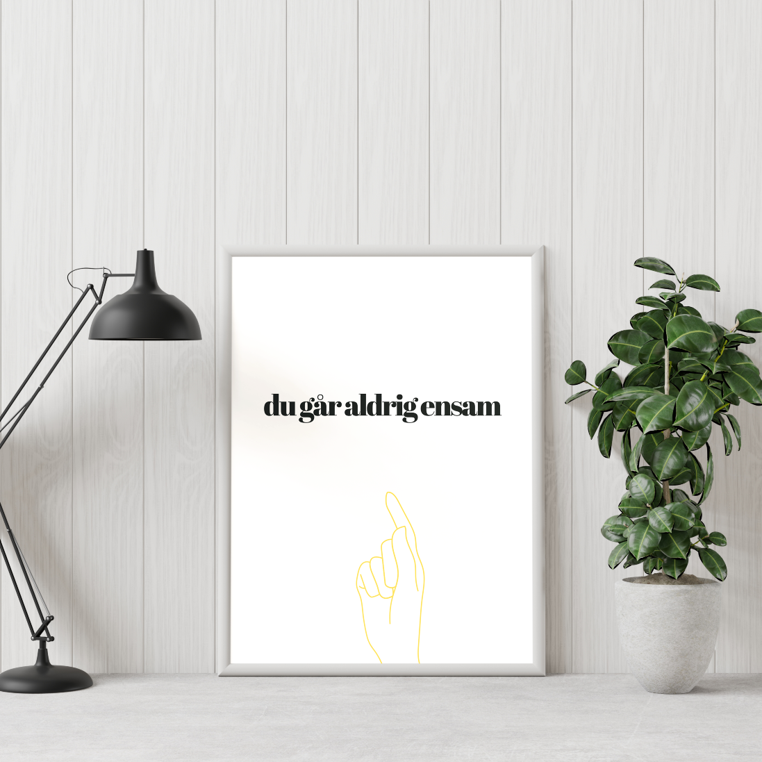 Poster Du går aldrig ensam mot vi vägg, grön växt till höger och skrivbordslampa till vänster