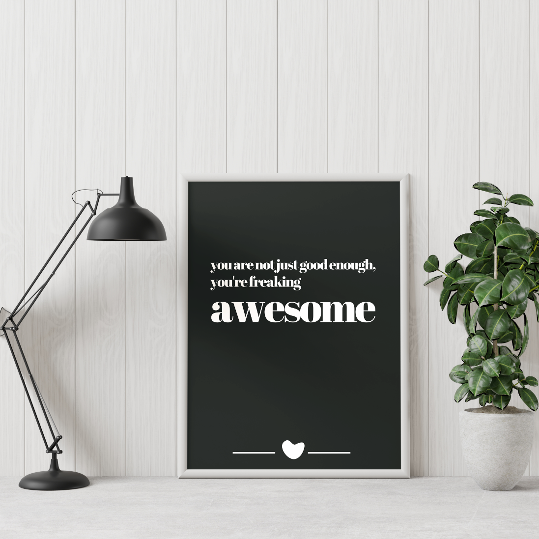 Poster freaking awesome inramad mot vit vägg. En grön växt till höger och skrivbordslampa till vänster