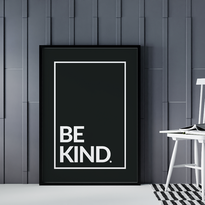 Poster Be kind, vita bokstäver mot svart bakgrund. Inramad och stående på golvet lutad mot grå vägg. En pinnstol syns till höger