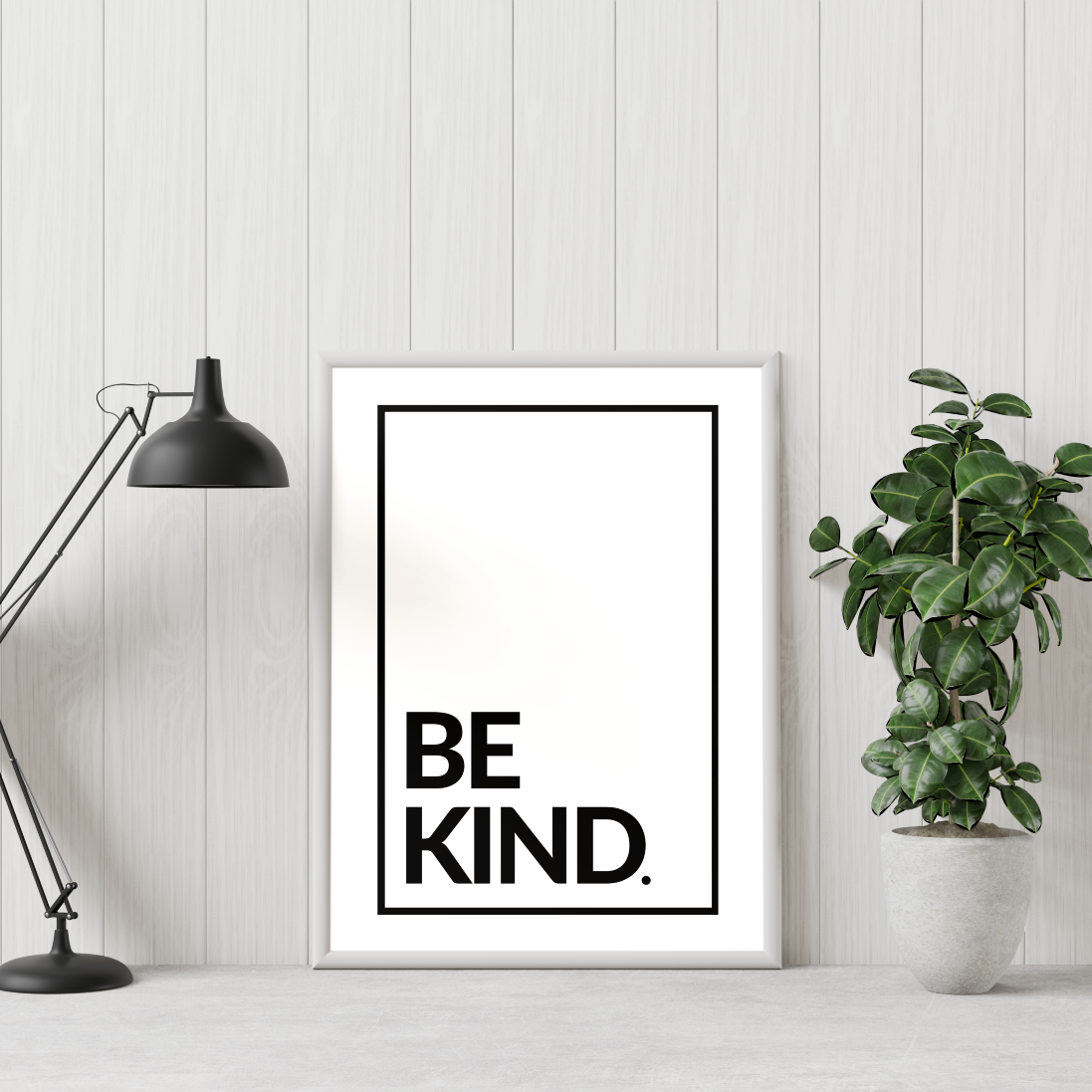 Poster Be kind svarta bokstäver mot vit bakgrund. Inramad, en grön växt står till höger och en skrivbordslampa till vänster