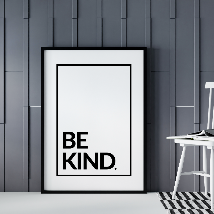 Poster Be kind, svart bokstäver mot vit bakrgrund. Inramad och lutande mot grå vägg, en pinnstol syns till höger