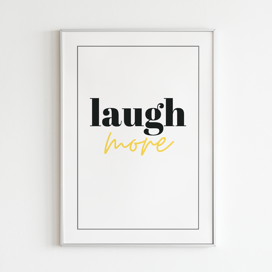 Poster Laugh more med goldfoliering på "more" inramad mot vit vägg