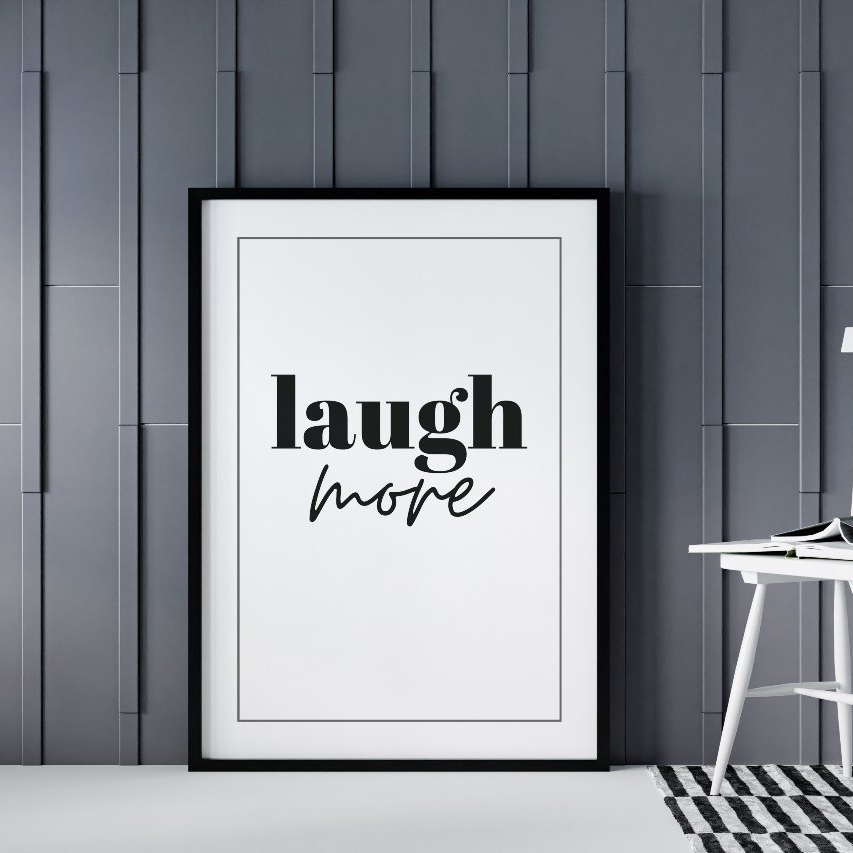 Poster Laugh more inramad mot grå vägg, till höger syns en vit stol