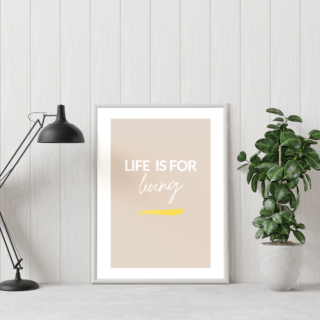 Poster Life is for living, med guldfoliering, inramad, till höger syns en grön växt och till vänster en skrivbordslampa