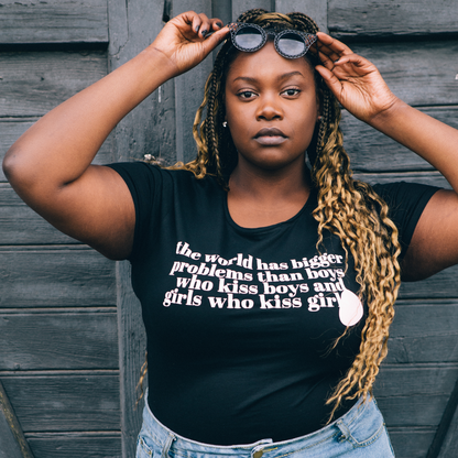 T-shirt The World has Bigger Problems modell framför gammal vägg av brädor, lyfter upp sina solglasögon i pannan