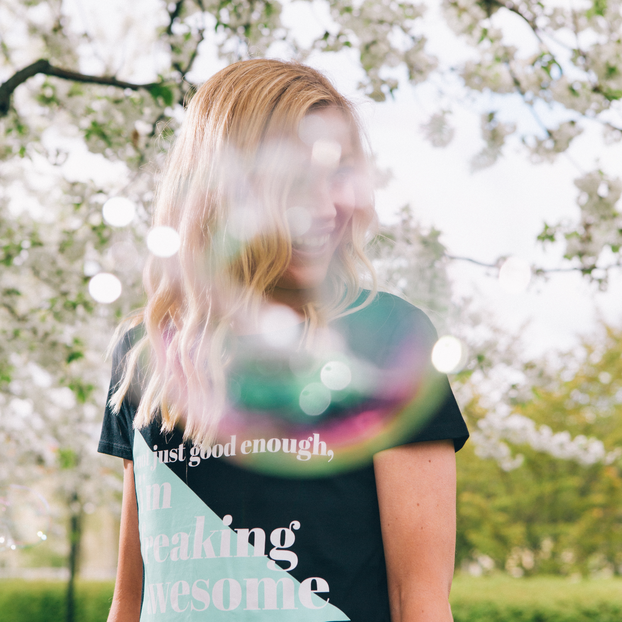 T-shirt Freaking Awesome, model under ett träd med vita blommor. Ansiktet skyms lätt av såpbubblor