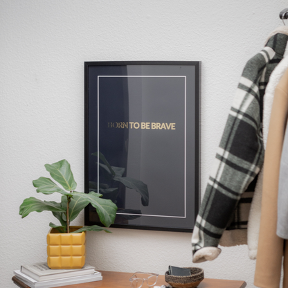 Poster Born to be brave. Inramad i typsik hallmiljö med ytterkläder och byrå med småsaker på